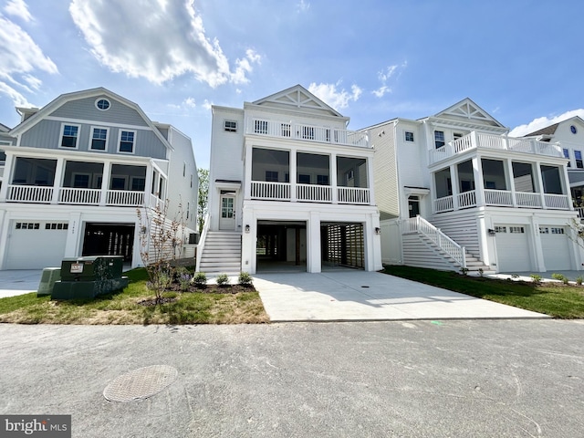 beach home featuring a sunroom, a balcony, stairway, and concrete driveway