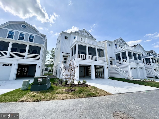 raised beach house with driveway, a sunroom, a garage, stairway, and a balcony