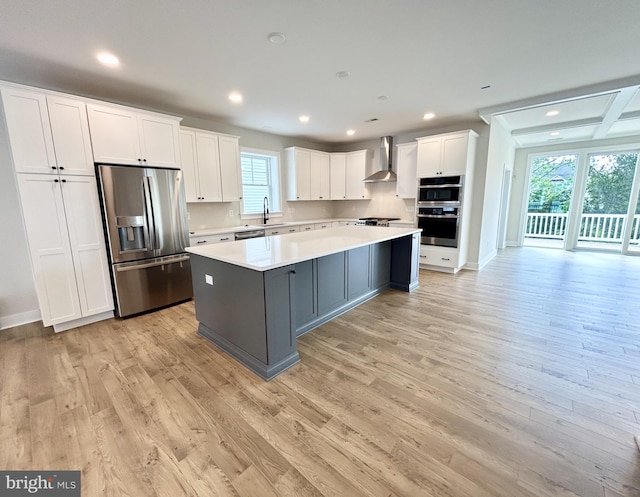 kitchen with appliances with stainless steel finishes, light countertops, wall chimney exhaust hood, white cabinetry, and a kitchen island