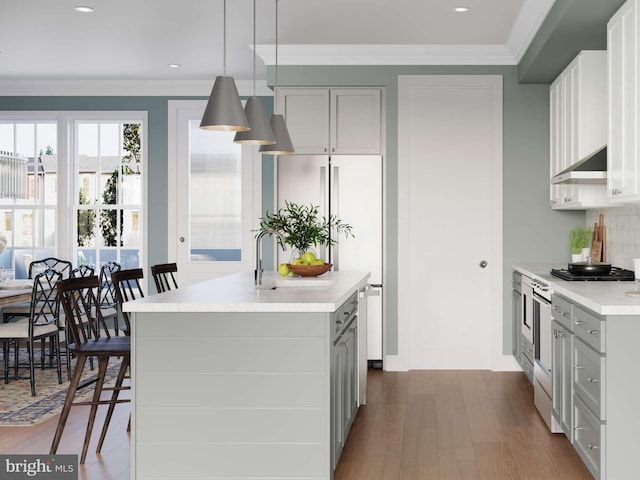 kitchen with dark wood-style flooring, decorative light fixtures, a center island with sink, a sink, and light countertops