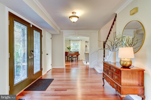 foyer entrance with french doors, arched walkways, light wood-type flooring, stairs, and crown molding