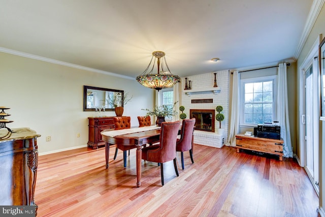 dining room featuring plenty of natural light, light wood-type flooring, a brick fireplace, ornamental molding, and baseboards