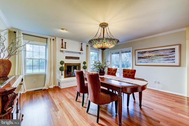 dining space with wood finished floors, baseboards, a brick fireplace, and crown molding