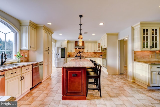 kitchen featuring stainless steel appliances, a sink, cream cabinets, decorative backsplash, and wall chimney exhaust hood