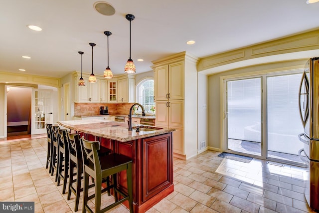 kitchen with a sink, cream cabinets, light stone counters, freestanding refrigerator, and glass insert cabinets