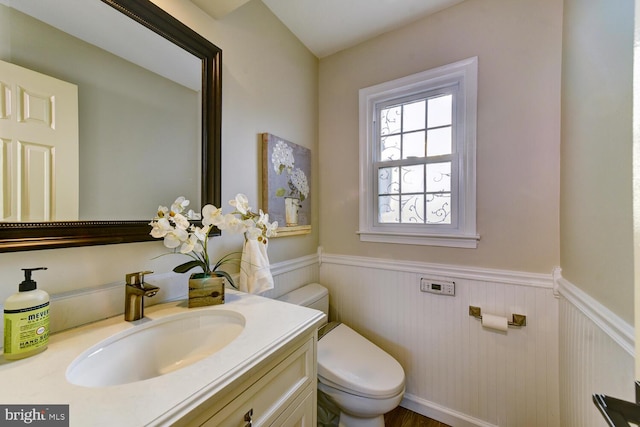 half bathroom with a wainscoted wall, toilet, and vanity
