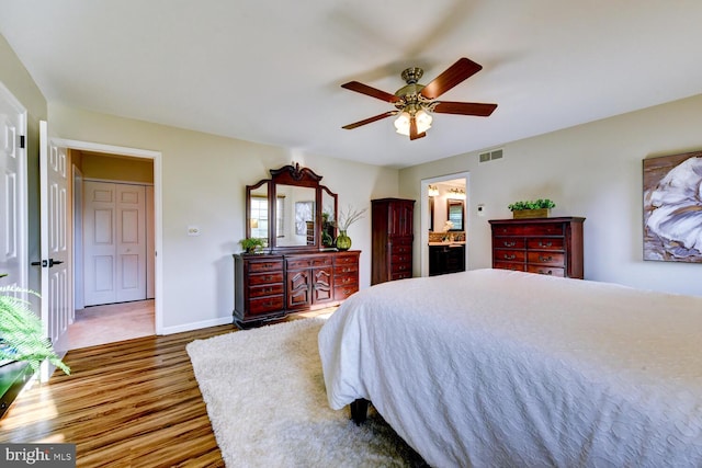 bedroom featuring wood finished floors, ensuite bath, baseboards, and a ceiling fan