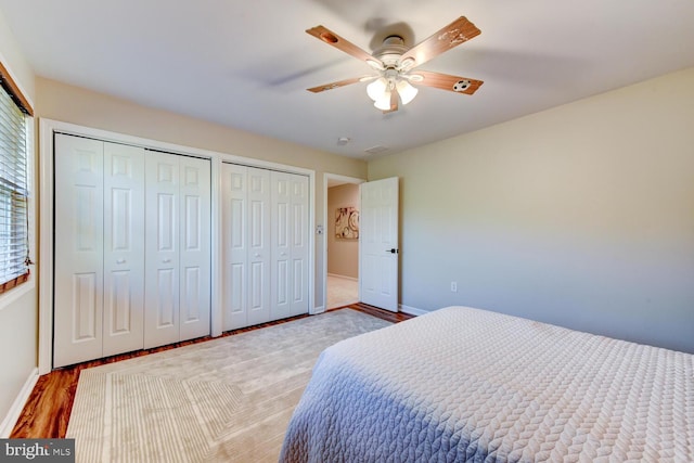bedroom featuring multiple closets, wood finished floors, baseboards, and a ceiling fan