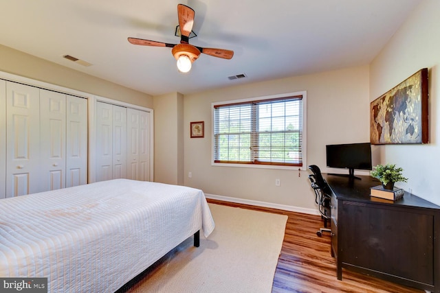 bedroom with wood finished floors, multiple closets, baseboards, a ceiling fan, and a desk