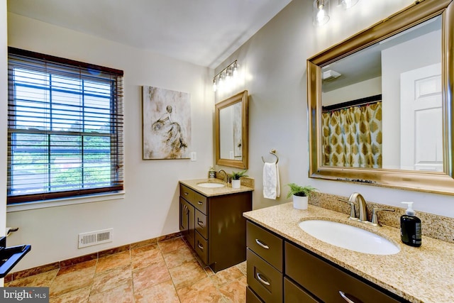 full bath with healthy amount of natural light, two vanities, and baseboards