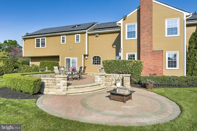 back of property featuring a patio area, a chimney, solar panels, a fire pit, and a lawn