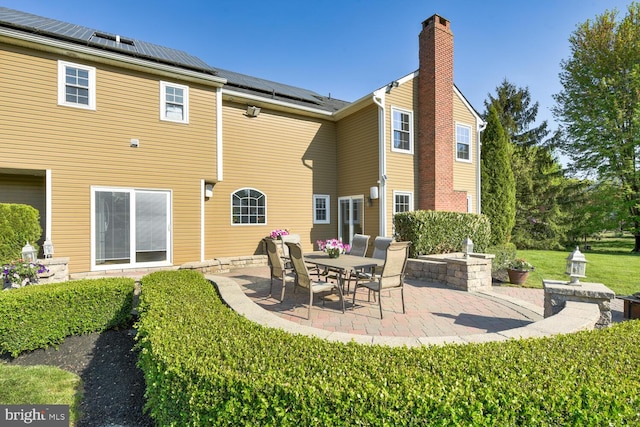 back of house with a patio, roof mounted solar panels, and a chimney