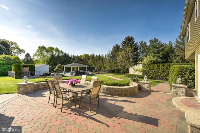 view of patio / terrace with a gazebo, outdoor dining space, an outbuilding, and view of wooded area