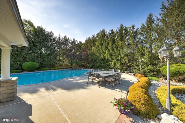 outdoor pool featuring a patio, outdoor dining area, and view of wooded area