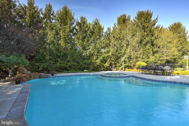view of swimming pool featuring a patio area, a pool with connected hot tub, and fence