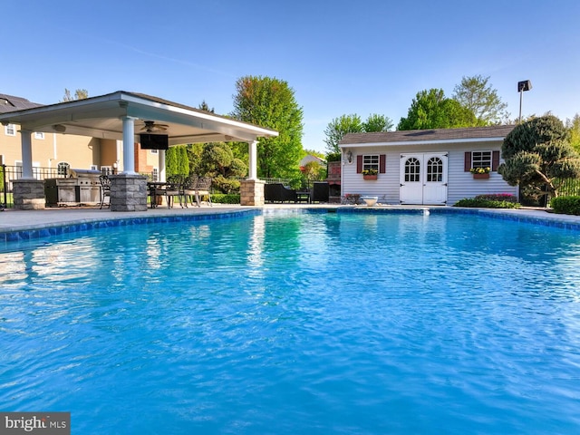 outdoor pool with exterior kitchen, ceiling fan, an outbuilding, fence, and a storage structure