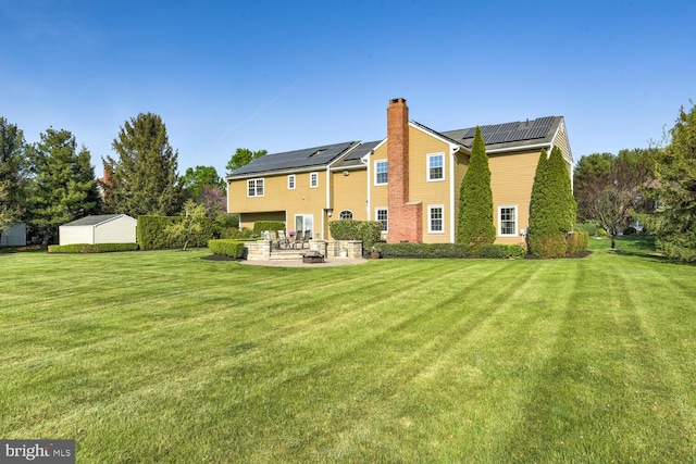 back of house with a patio area, solar panels, a lawn, and a chimney