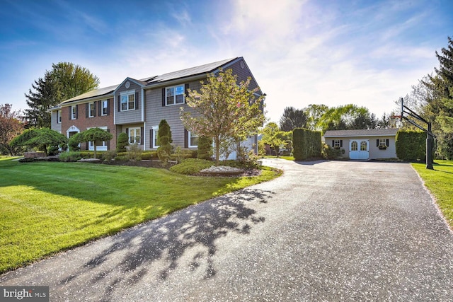 view of front of house with driveway, roof mounted solar panels, and a front yard