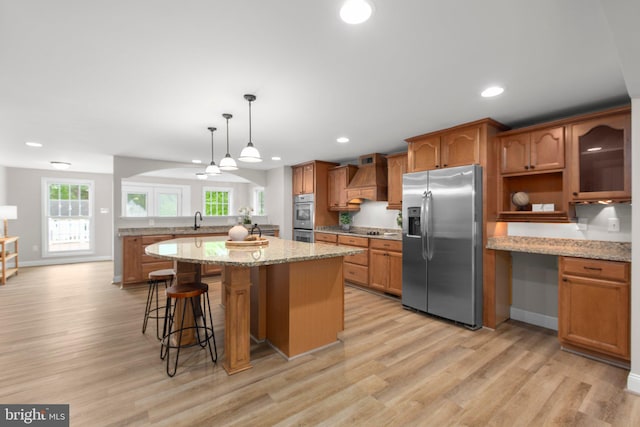 kitchen featuring appliances with stainless steel finishes, light wood finished floors, a kitchen breakfast bar, brown cabinetry, and recessed lighting