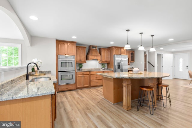 kitchen featuring a breakfast bar area, premium range hood, light wood-type flooring, a sink, and appliances with stainless steel finishes