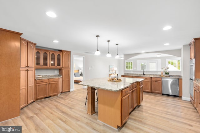 kitchen featuring light wood-style floors, a breakfast bar area, dishwasher, brown cabinetry, and a center island