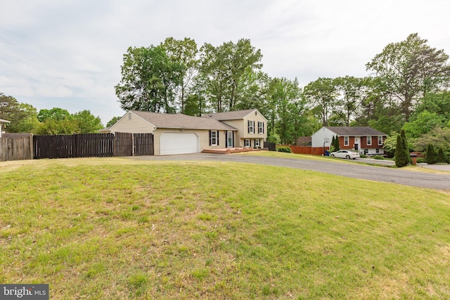 tri-level home featuring an attached garage, fence, a front lawn, and aphalt driveway