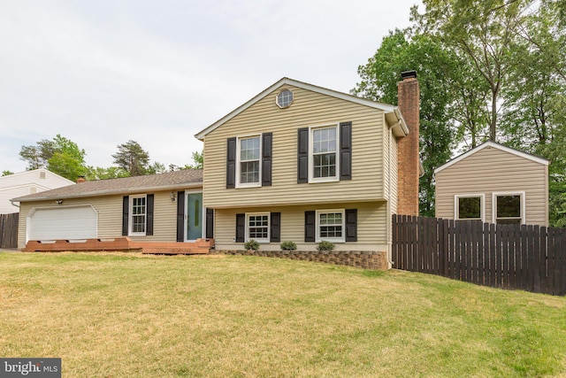 tri-level home with an attached garage, fence, a chimney, and a front lawn