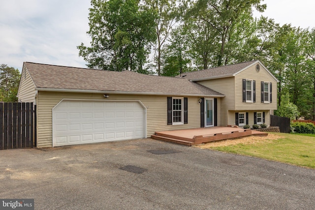 split level home with a shingled roof, fence, driveway, and a deck