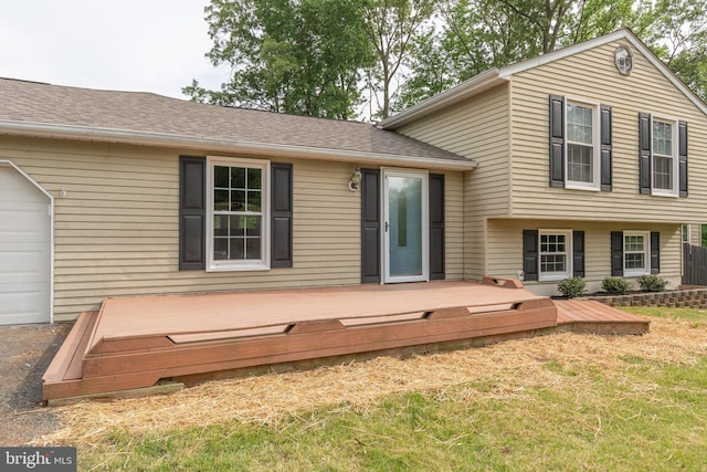 back of property featuring an attached garage, a lawn, and a deck