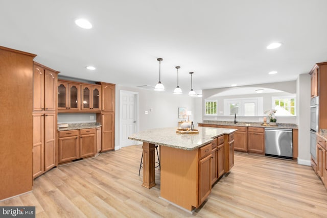 kitchen with a breakfast bar area, brown cabinetry, arched walkways, light wood-type flooring, and dishwasher