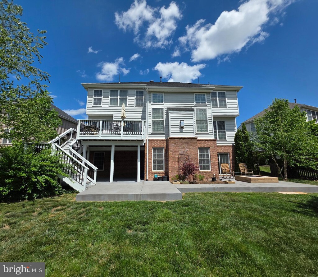 rear view of house with a deck, a patio, brick siding, a yard, and stairway