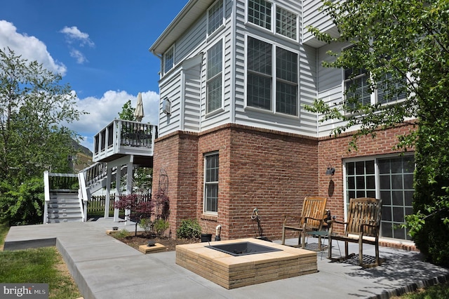 view of property exterior with stairs, a patio area, a wooden deck, and an outdoor fire pit