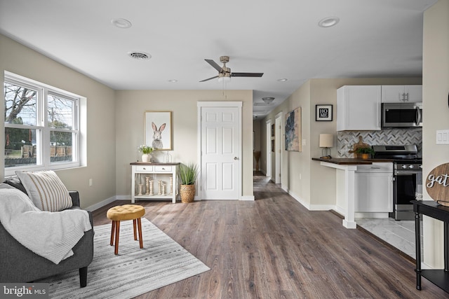 living room featuring baseboards, a ceiling fan, wood finished floors, and visible vents