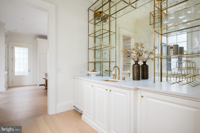 bar with a sink, baseboards, crown molding, and light wood finished floors
