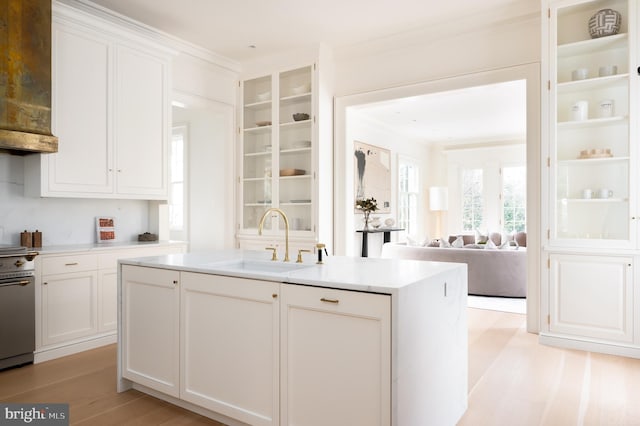 kitchen with white cabinets, a sink, a kitchen island with sink, light countertops, and range