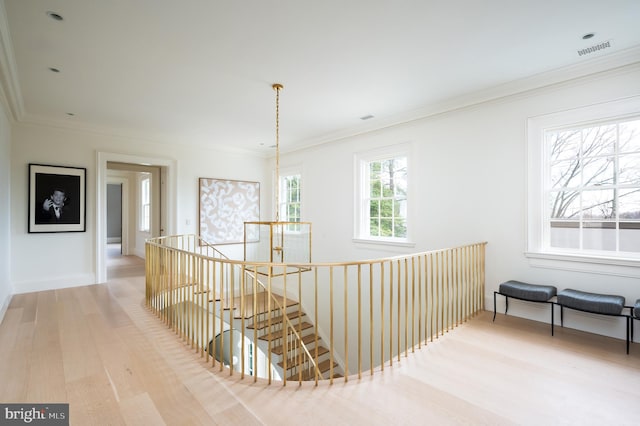 hallway with visible vents, crown molding, wood finished floors, baseboards, and an upstairs landing