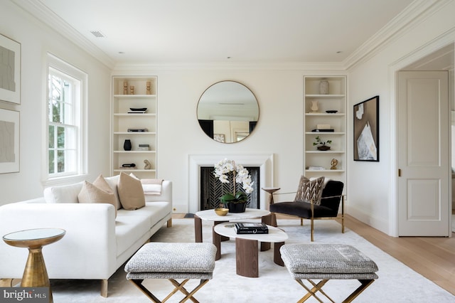 living room with visible vents, crown molding, built in features, a fireplace, and light wood-style flooring