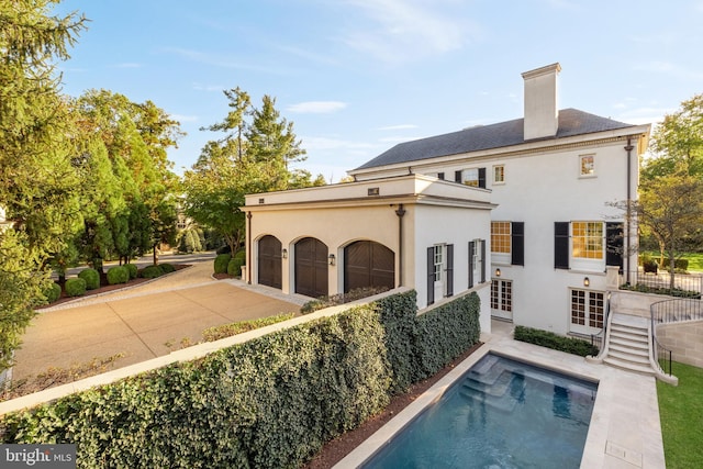 back of house with a garage, an outdoor pool, stucco siding, a chimney, and concrete driveway