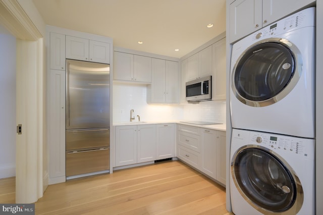 laundry area with laundry area, stacked washing maching and dryer, recessed lighting, a sink, and light wood finished floors