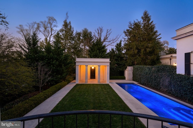 pool at dusk with a fenced in pool, an outdoor structure, and a lawn