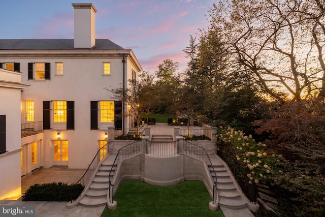 rear view of house featuring a chimney, stucco siding, a patio area, and stairway