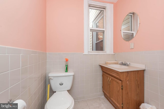 bathroom with tile walls, a wainscoted wall, vanity, and toilet