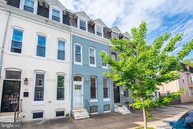 townhome / multi-family property featuring brick siding, mansard roof, a residential view, and entry steps