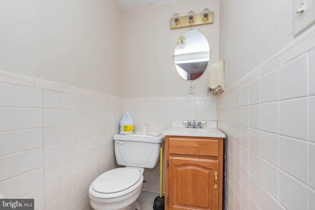 half bathroom with tile walls, a wainscoted wall, vanity, and toilet