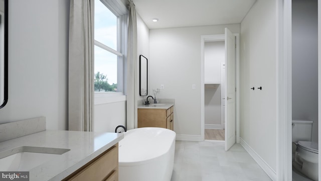 full bath with toilet, baseboards, two vanities, a soaking tub, and a sink