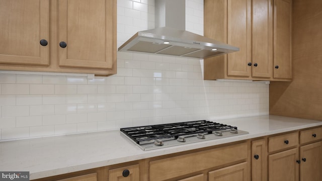 kitchen with light stone counters, decorative backsplash, wall chimney exhaust hood, and stainless steel gas stovetop