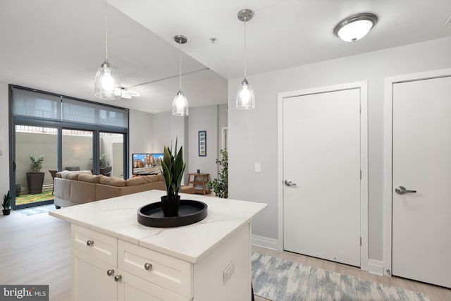 kitchen with a kitchen island, pendant lighting, light stone countertops, light wood-type flooring, and white cabinets