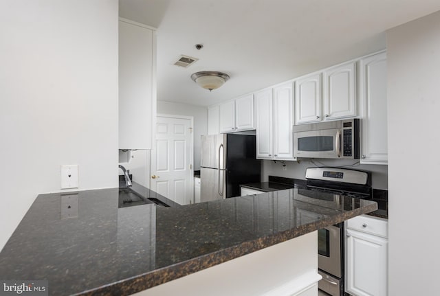 kitchen with white cabinets, appliances with stainless steel finishes, and dark stone countertops