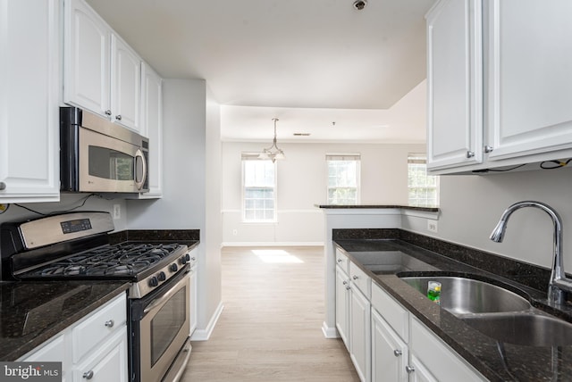 kitchen featuring a sink, light wood finished floors, dark stone counters, stainless steel appliances, and white cabinetry