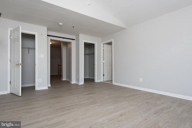 unfurnished bedroom with multiple closets, baseboards, a spacious closet, and light wood-type flooring